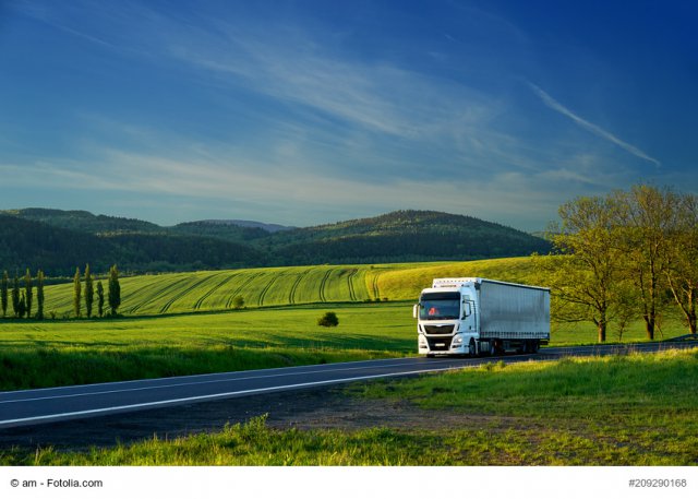 White truck driving on the asphalt road in a rural landscape with forested mountains in the background